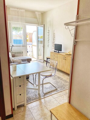 Quarto moderno e bem iluminado, com mesa de jantar, cadeiras, sofá e televisão.