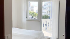 Een slaapkamer met een bed, een raam en uitzicht op gebouwen.