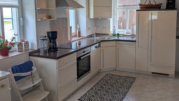 A modern kitchen with white cabinetry, a built-in oven, a coffee maker, and a window with blinds.