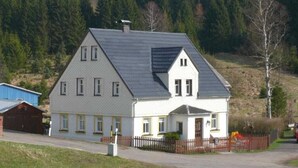 A two-story house with a gabled roof, a front porch, and a fenced yard.