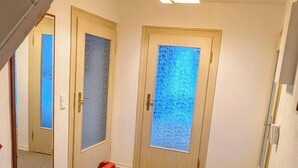 A hallway with carpeted floors, wooden doors with frosted glass panels, and a red railing.
