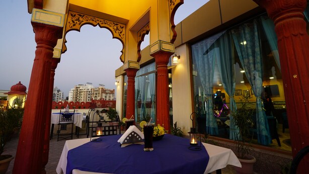 An outdoor dining area with a table set for two, surrounded by ornate columns and potted plants.