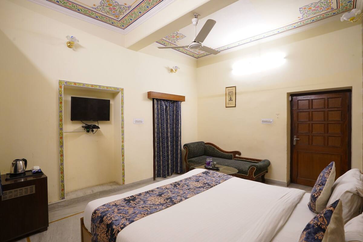 Une chambre d’hôtel avec un lit, un canapé, une télévision, un ventilateur de plafond et une porte.
