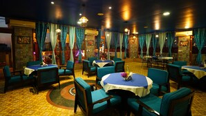 A restaurant with round tables and chairs, teal curtains, and patterned carpet.
