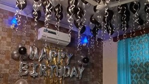 A bedroom with a bed, a wall-mounted air conditioner, and a ceiling with hanging balloons.