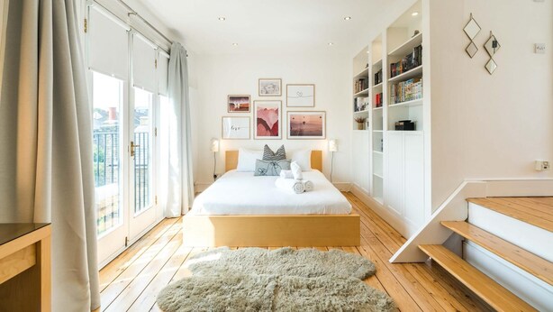 A modern bedroom with a large bed, a wooden floor, a fluffy rug, a bookshelf, and a staircase.
