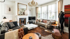 A living room with a fireplace, a television, a sofa, a coffee table, and a chandelier.