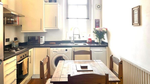 A compact kitchen with a stove, oven, microwave, and washing machine. There is a sink, a window, and a table with chairs. - 2 Bed Self Contained Apartment Wrexham (Wrexham)