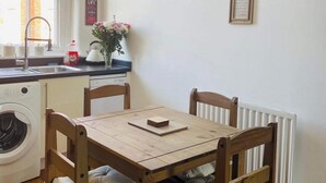 A dining area with a wooden table and four chairs, a washing machine, a radiator, and a clock on the wall. - 2 Bed Self Contained Apartment Wrexham (Wrexham)