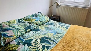 A bed with a tropical leaf pattern bedspread, a yellow blanket, and a bedside lamp. - 2 Bed Self Contained Apartment Wrexham (Wrexham)