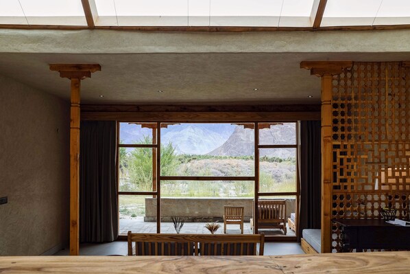 A room with a large window, wooden furniture, and a view of mountains.
