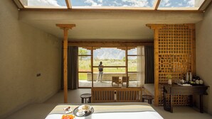 Una camera d'albergo con un'ampia finestra, un letto, un tavolo imbandito per la colazione e vista sulle montagne.