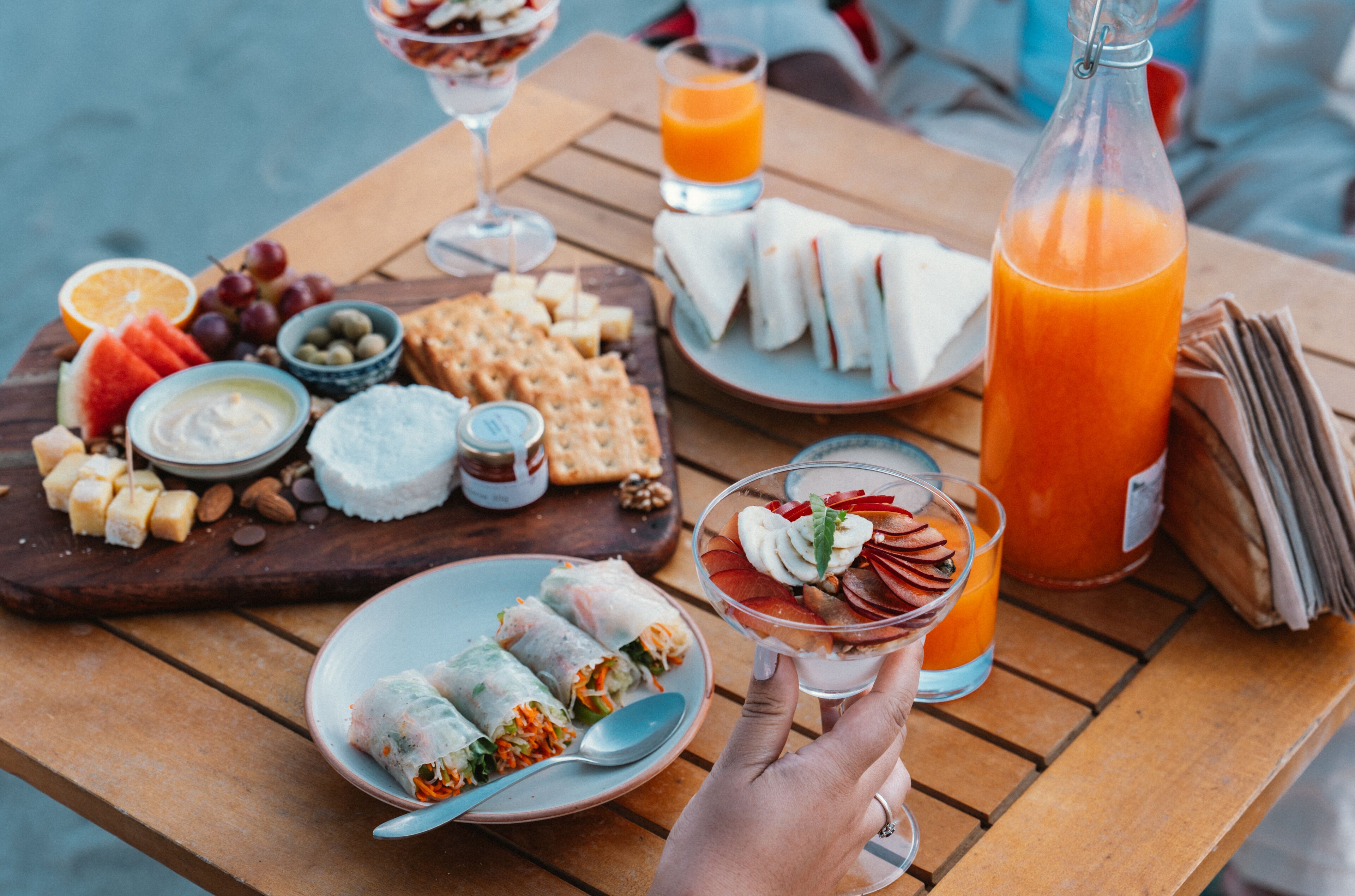 A wooden table with a variety of food items including sandwiches, fruits, and a bottle of orange juice.