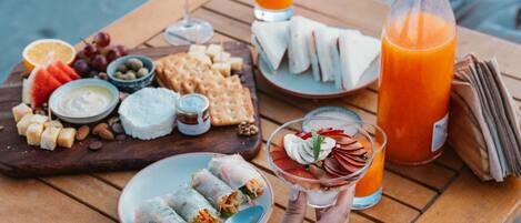A wooden table with a variety of food items including sandwiches, fruits, and a bottle of orange juice.