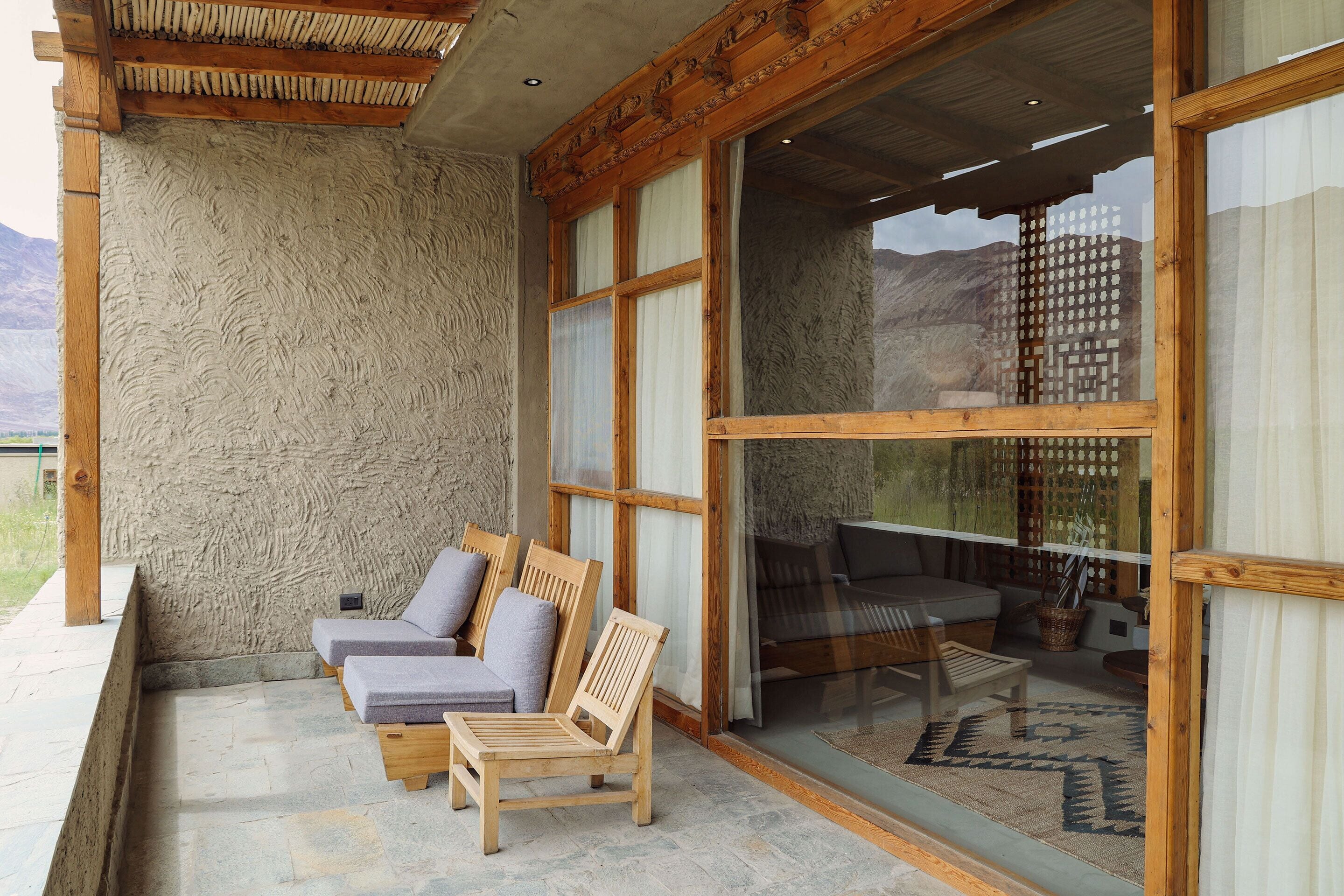 A cozy outdoor seating area with wooden chairs and cushions, large windows, and a view of the mountains.