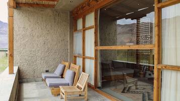 A cozy outdoor seating area with wooden chairs and cushions, large windows, and a view of the mountains.
