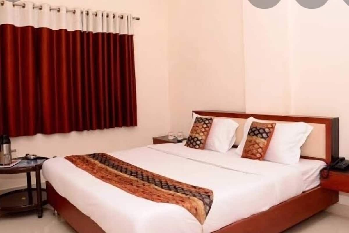 A hotel room with a bed, a bedside table, a nightstand, a red curtain, and a wall socket.