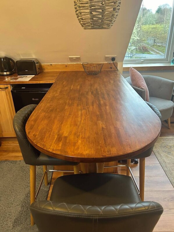 Une cuisine moderne avec une table à manger en bois, des chaises noires et une vue sur l’extérieur.
