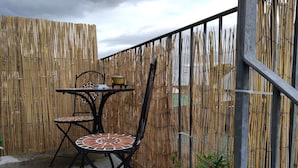 Une terrasse extérieure avec une table en métal et deux chaises, une clôture en bambou et une rambarde en métal.