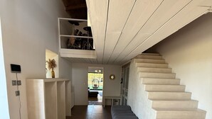 Um corredor espaçoso com uma escadaria à direita, um banco e uma planta à esquerda.