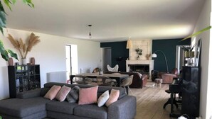 Uma sala moderna com um sofá seccional cinza, um espaço de refeições com mesa e cadeiras, uma lareira e um piano.