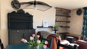 Ein Essbereich mit Tisch, Stühlen, einer Tulpenvase, einem schwarzen Klavier, einer Wanduhr und einem Regal mit einer Pflanze.