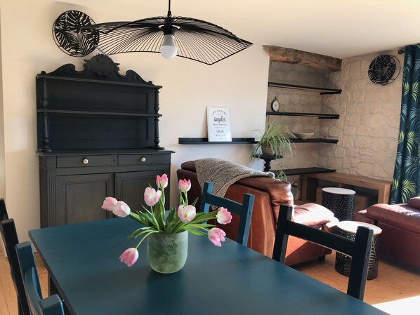 A dining area with a table, chairs, a vase of tulips, a black piano, a wall clock, and a shelf with a plant.