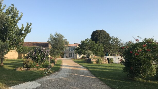 Ein Kiesweg führt zu einem Steinhaus mit Ziegeldach, umgeben von gepflegten Gärten und Bäumen.