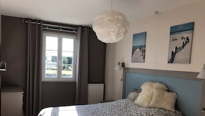 Ein Schlafzimmer mit einem Bett, einem Fenster mit Vorhängen, einem Heizkörper, einer Wandlampe und zwei gerahmten Bildern.