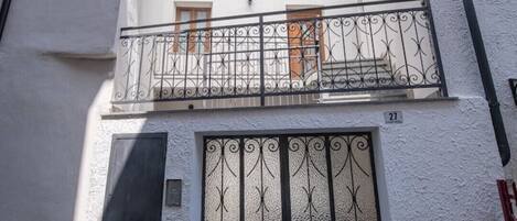 A two-story building with a balcony, a metal gate, and a small window.