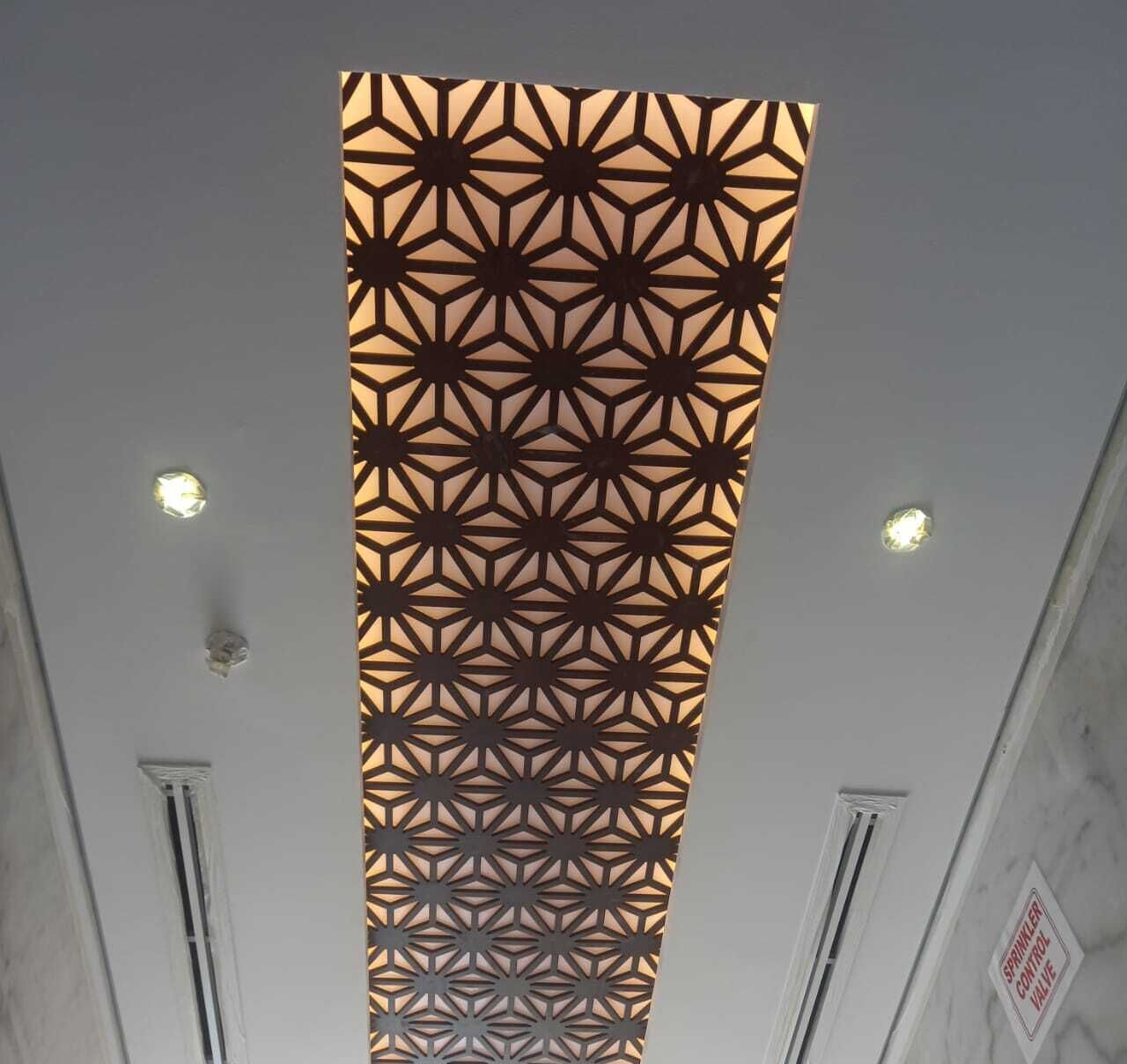 A ceiling with a geometric patterned panel and two visible air vents.