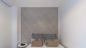 Ein kleines, aufgeräumtes Schlafzimmer mit einem Bett, Kissen und einem kleinen runden Tisch mit einem Hut.