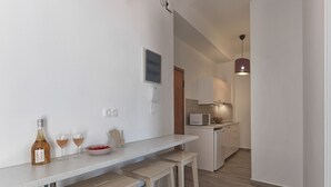 Eine kleine Küche mit weißer Arbeitsplatte, einer Mikrowelle und einem Spülbecken. Auf der Arbeitsplatte stehen zwei Hocker und eine Weinflasche.