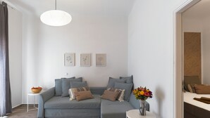 Ein modernes Wohnzimmer mit einem grauen Sofa, einem kleinen runden Tisch und einer Blumenvase sowie einer hängenden Leuchte.