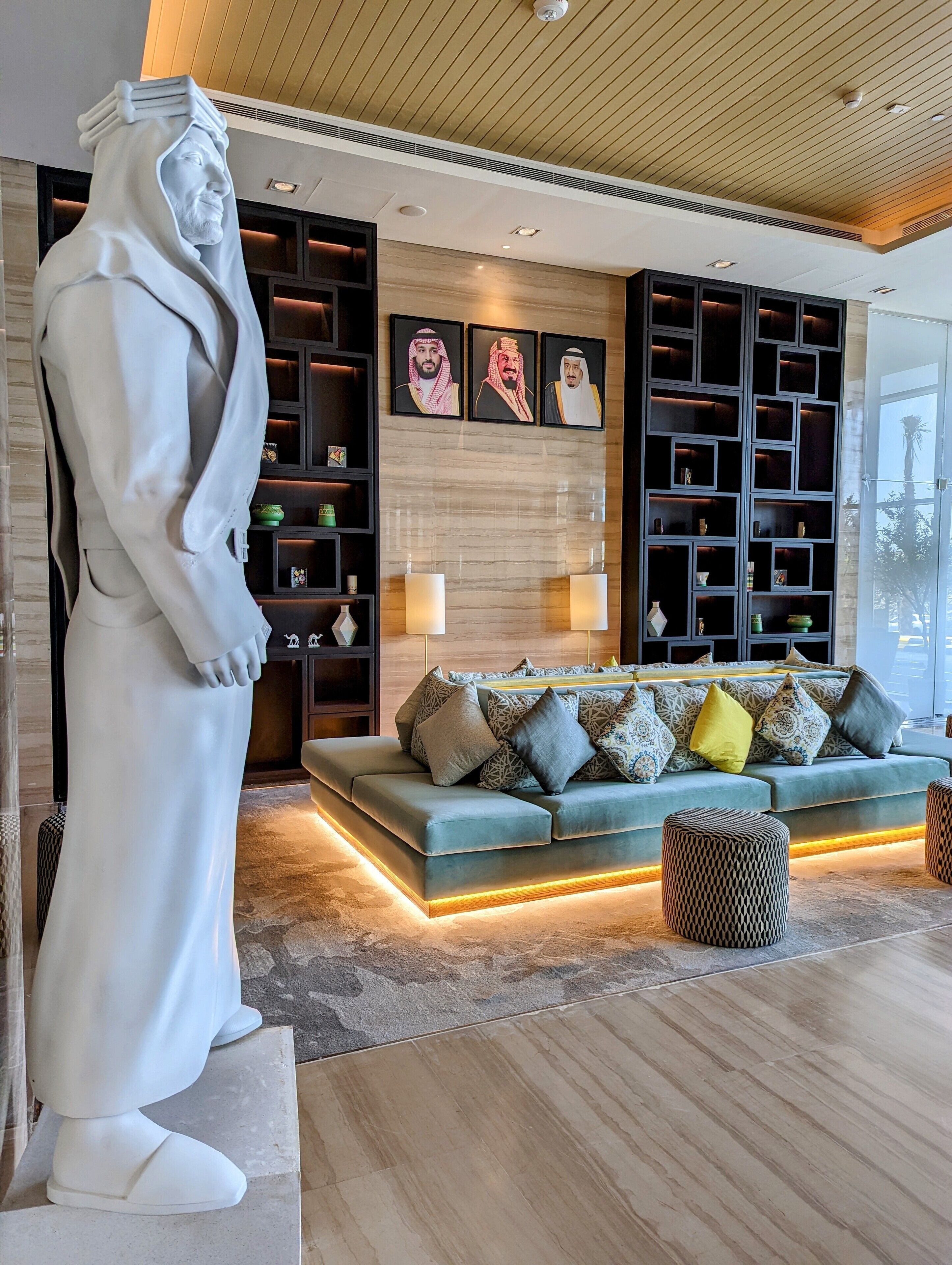 Un salon moderne avec une grande statue blanche, un canapé d’angle agrémenté de coussins à motifs et un mur orné de portraits encadrés.