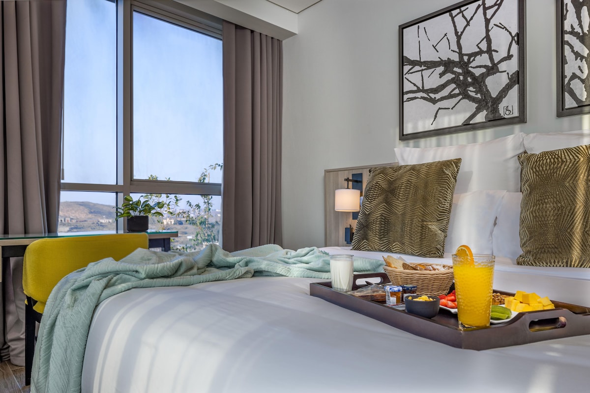 Una habitación de hotel con cama, bandeja de desayuno y ventana con cortinas.