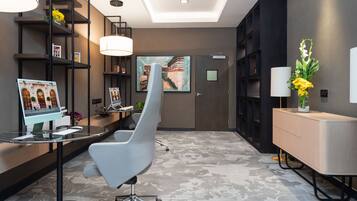 Un área de recepción moderna con un escritorio, una silla gris, un cuadro grande y una estantería.