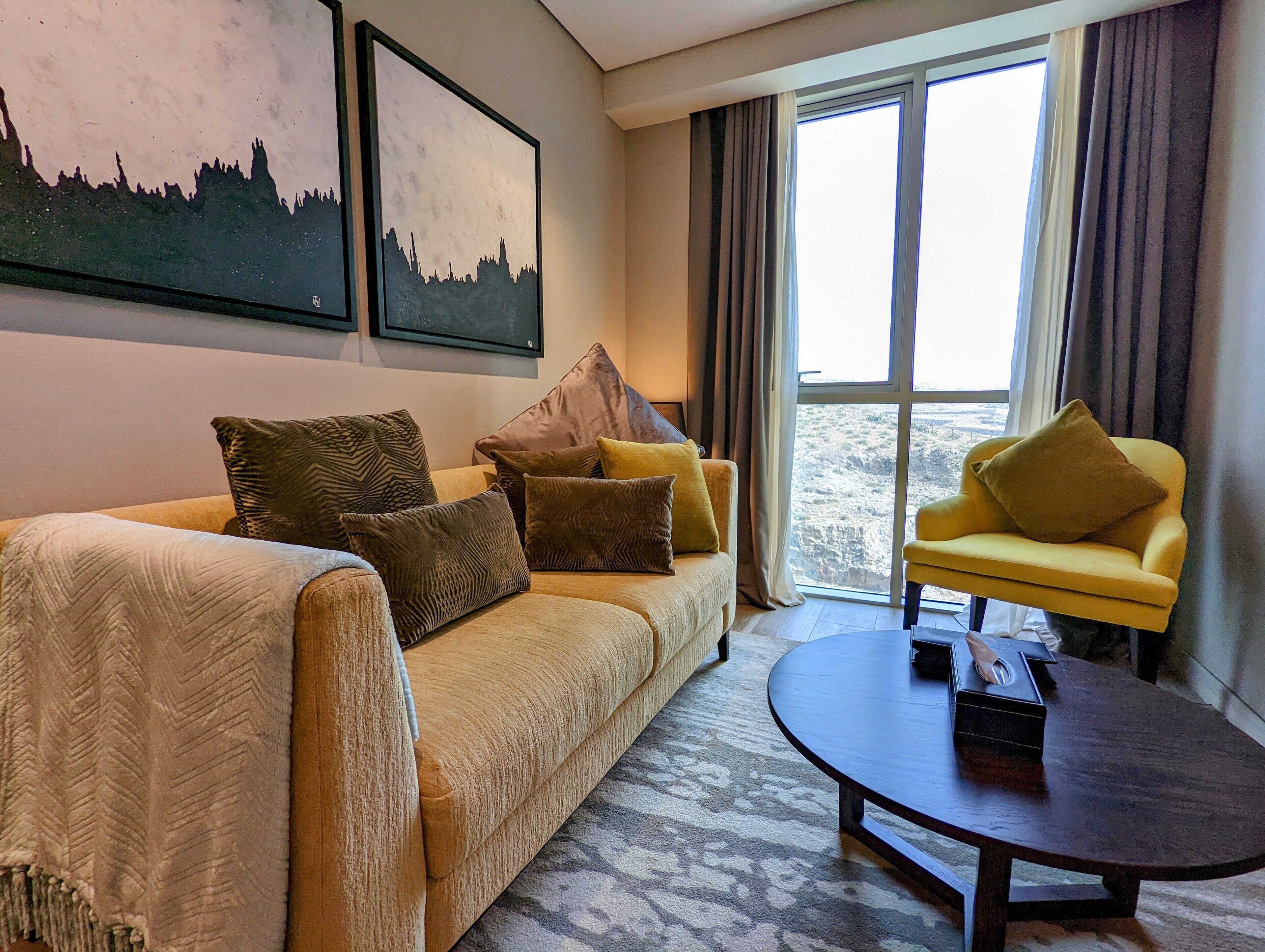 Ein Hotelzimmer mit einer Couch, einem gelben Sessel, einem runden Couchtisch und zwei gerahmten Bildern an der Wand.