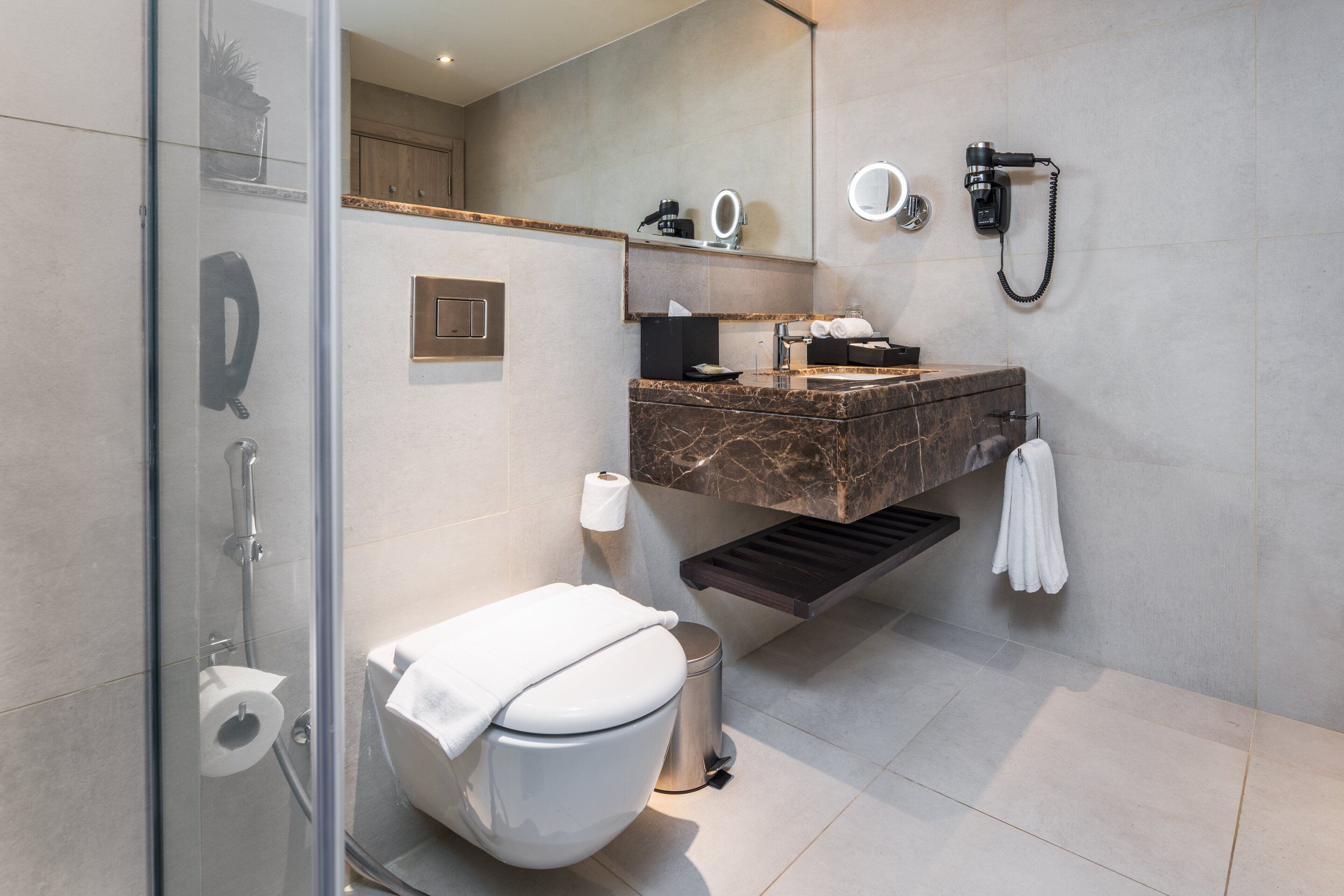 Un baño moderno con cabina de ducha de vidrio, lavamanos de mármol, inodoro y barra para toallas.