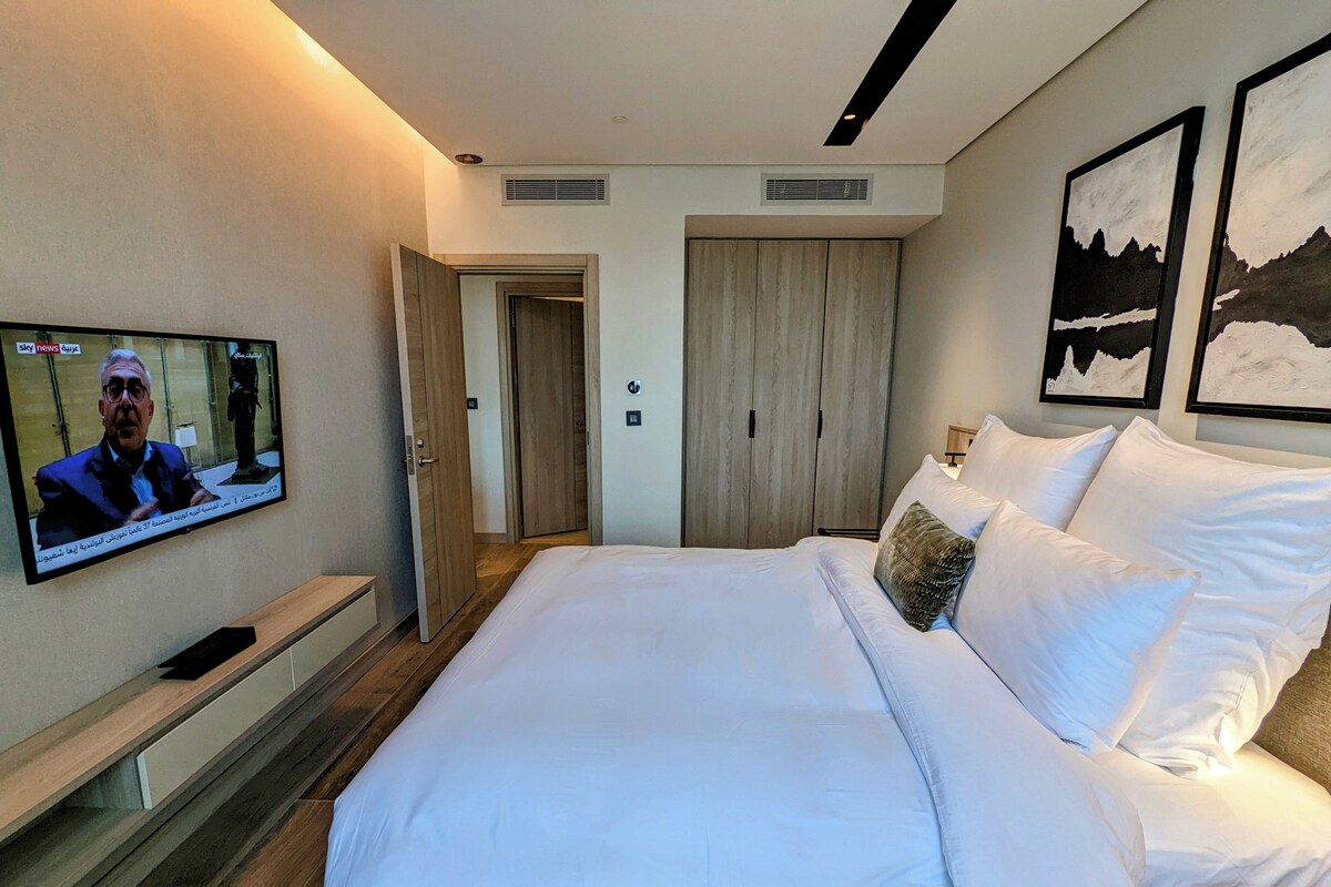 A hotel room with a large bed, a TV on the wall, and a wardrobe.