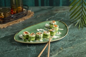 Un plato de sushi con rollos sobre un plato de cerámica verde, junto a palillos sobre una superficie de mármol.
