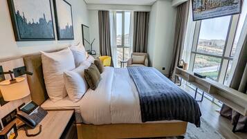 Una habitación de hotel moderna con una cama grande, teléfono junto a la cama y vistas a la ciudad a través de amplios ventanales.