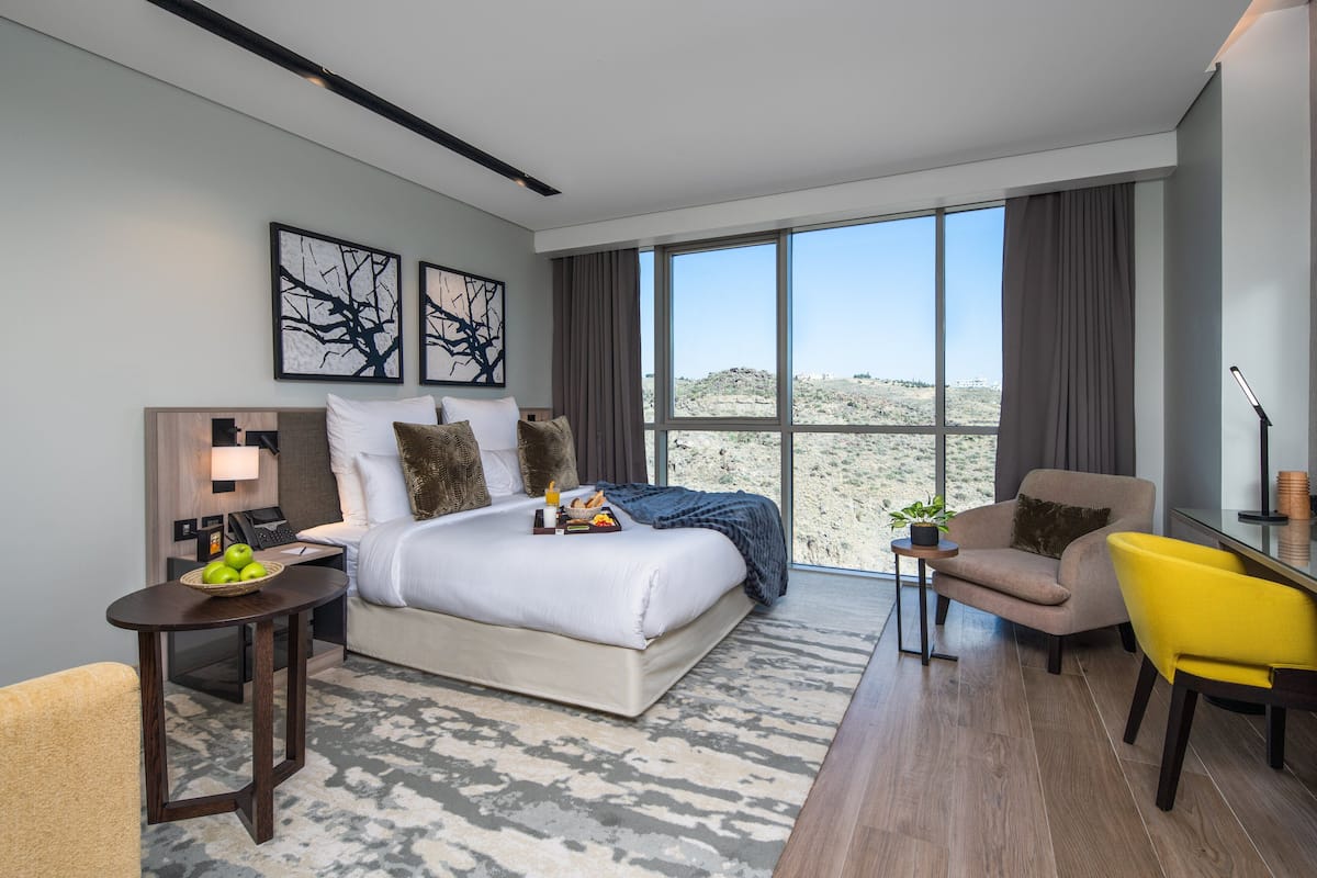 A modern hotel room with a large bed, a desk, a chair, and a view of the desert.