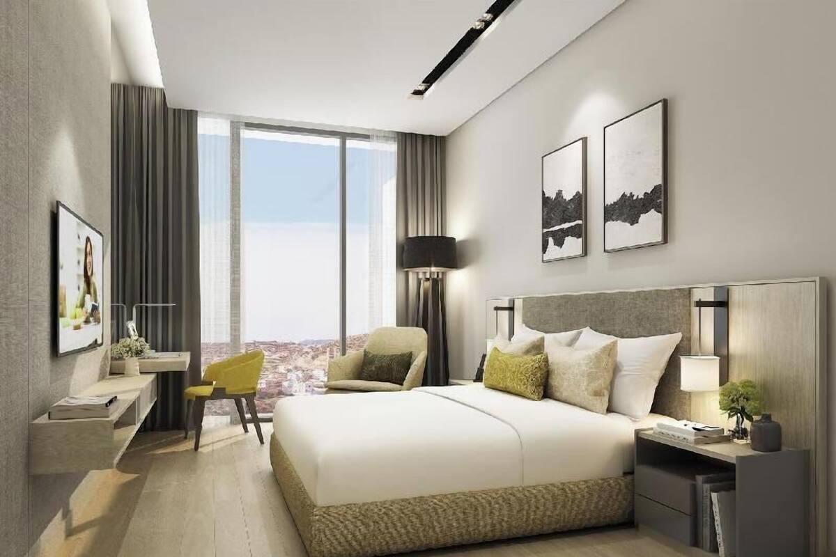 A modern hotel room with a large bed, a desk, a chair, and a view of the cityscape.