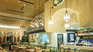 A restaurant interior with wooden ceiling, hanging pendant lights, and a bar area with shelves of bottles. - Citadines Abha (Abha)