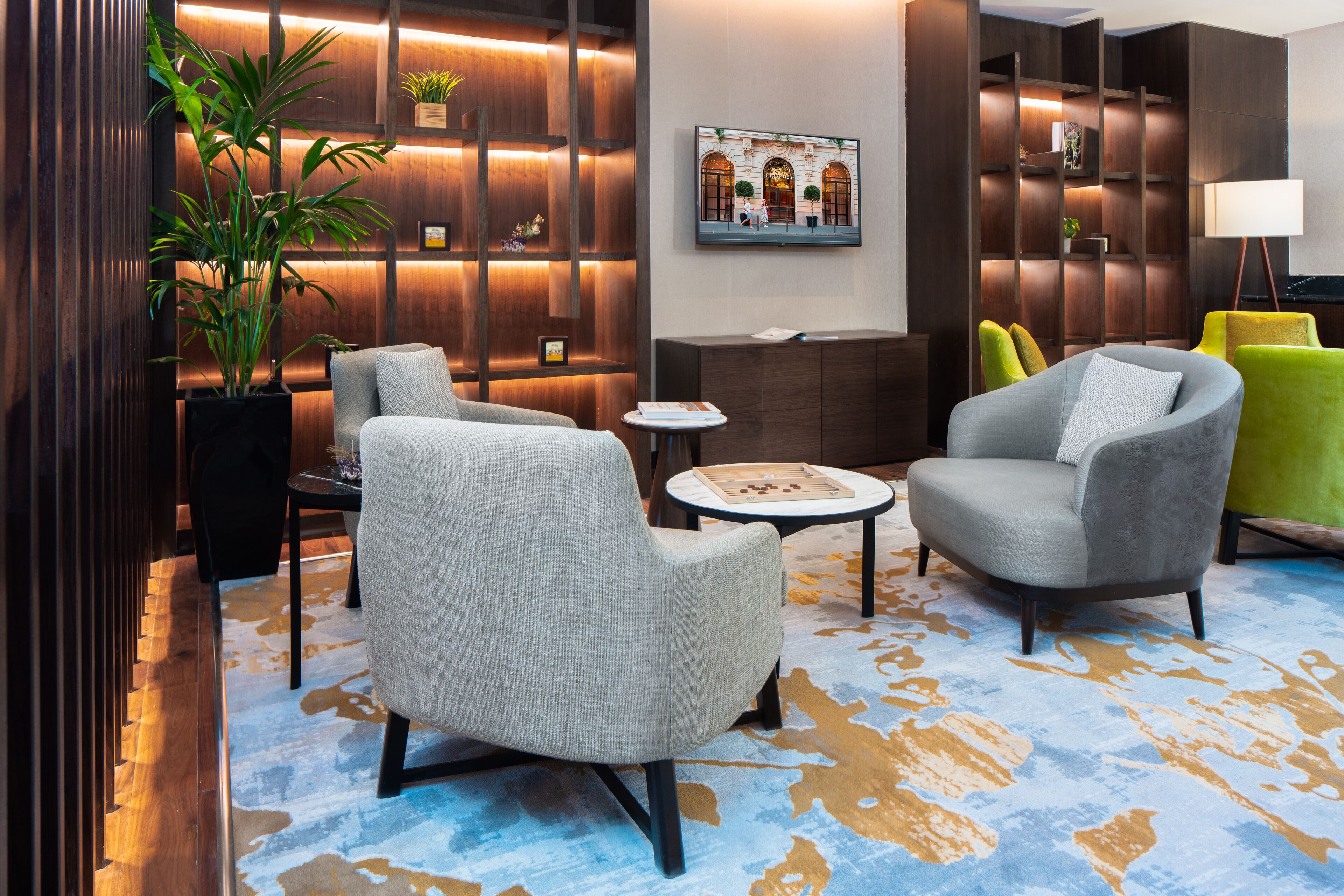 A modern lobby with a seating area featuring two grey armchairs, a small round table, and a potted plant.