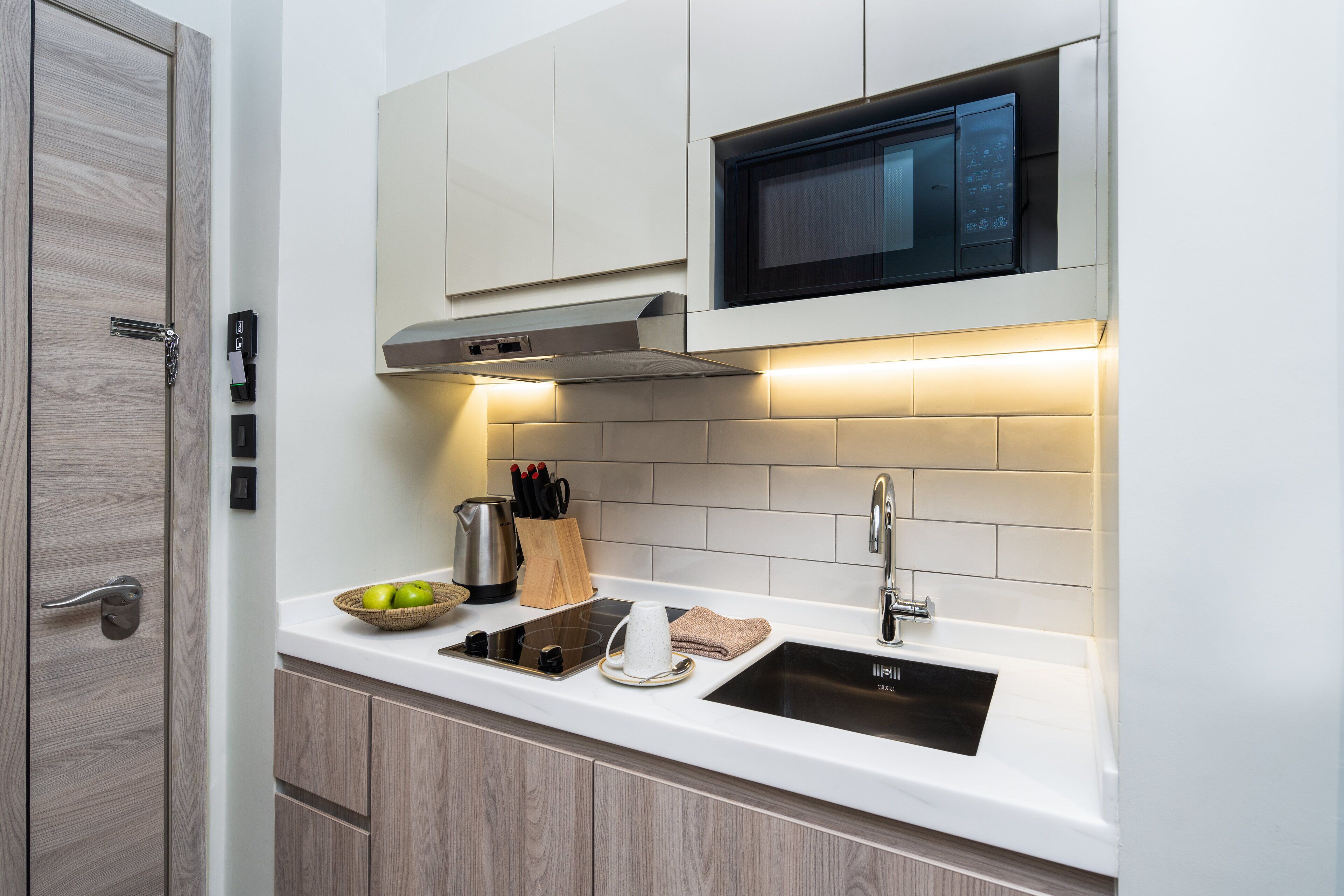 A modern kitchen with a microwave, stove, and sink. There is a wooden door and a set of knives on the counter.