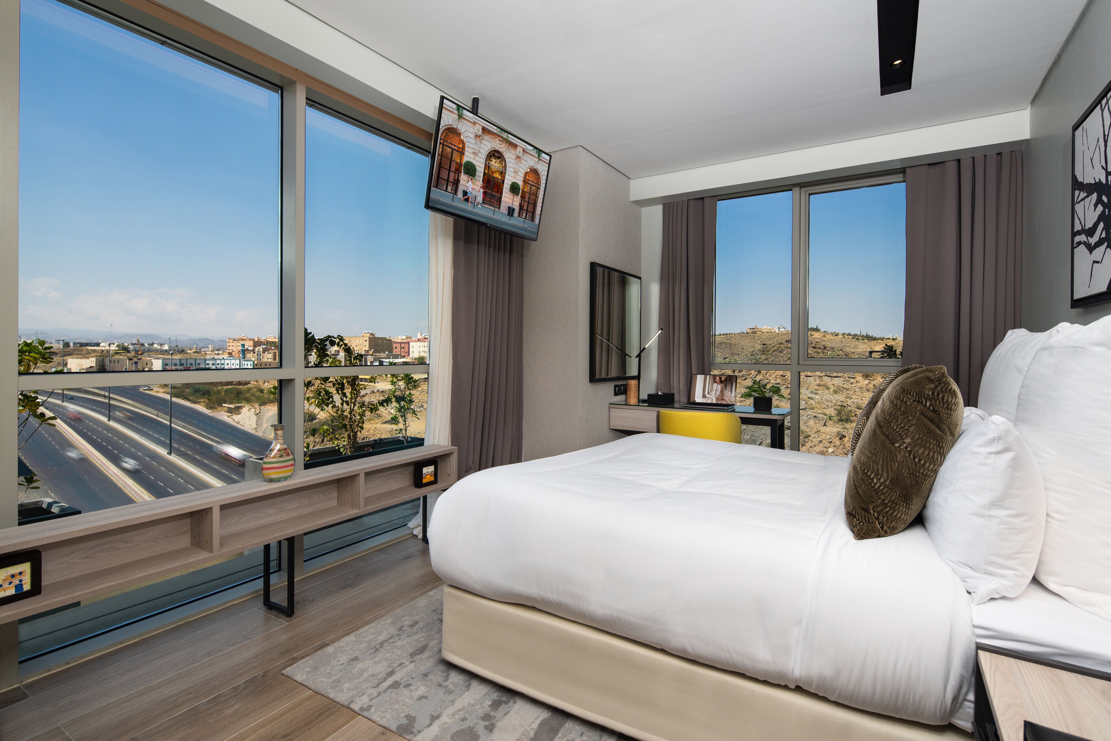 Una habitación de hotel moderna con una cama grande, un televisor montado en la pared y vistas a un paisaje desértico.