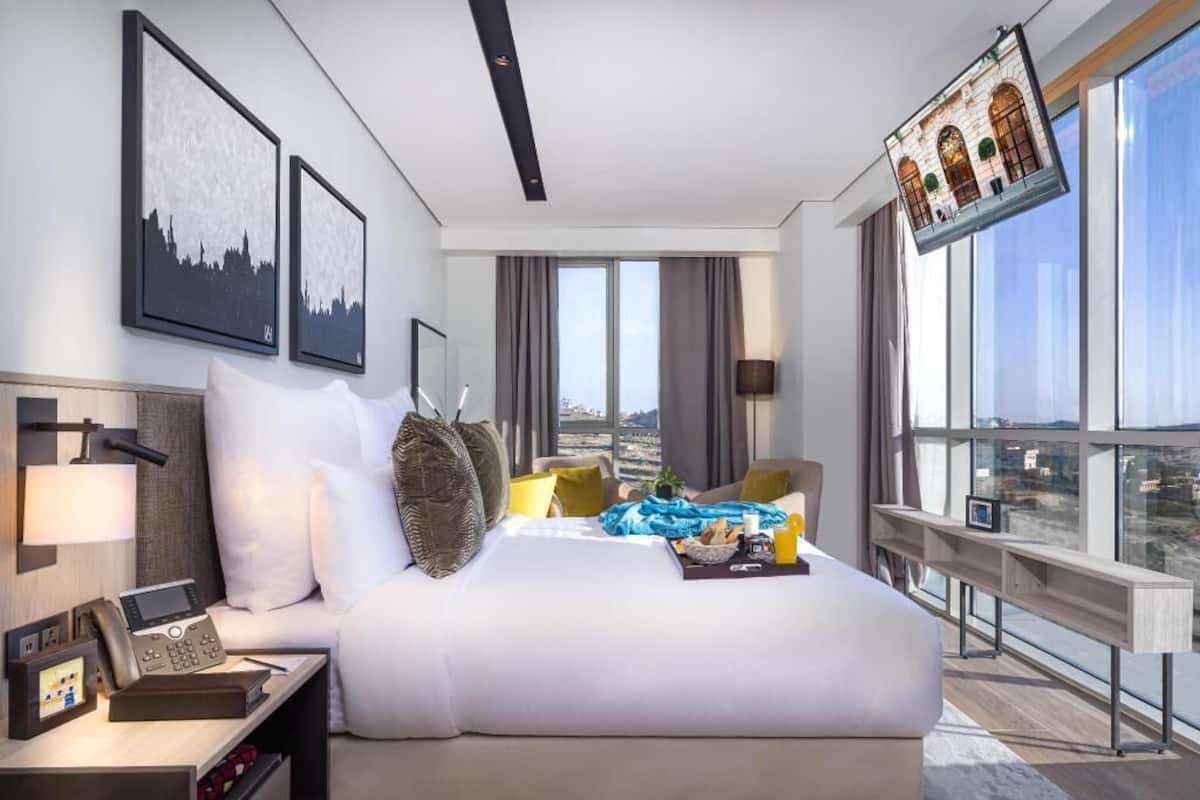 A modern hotel room with a large bed, a desk with a phone, and a city view.
