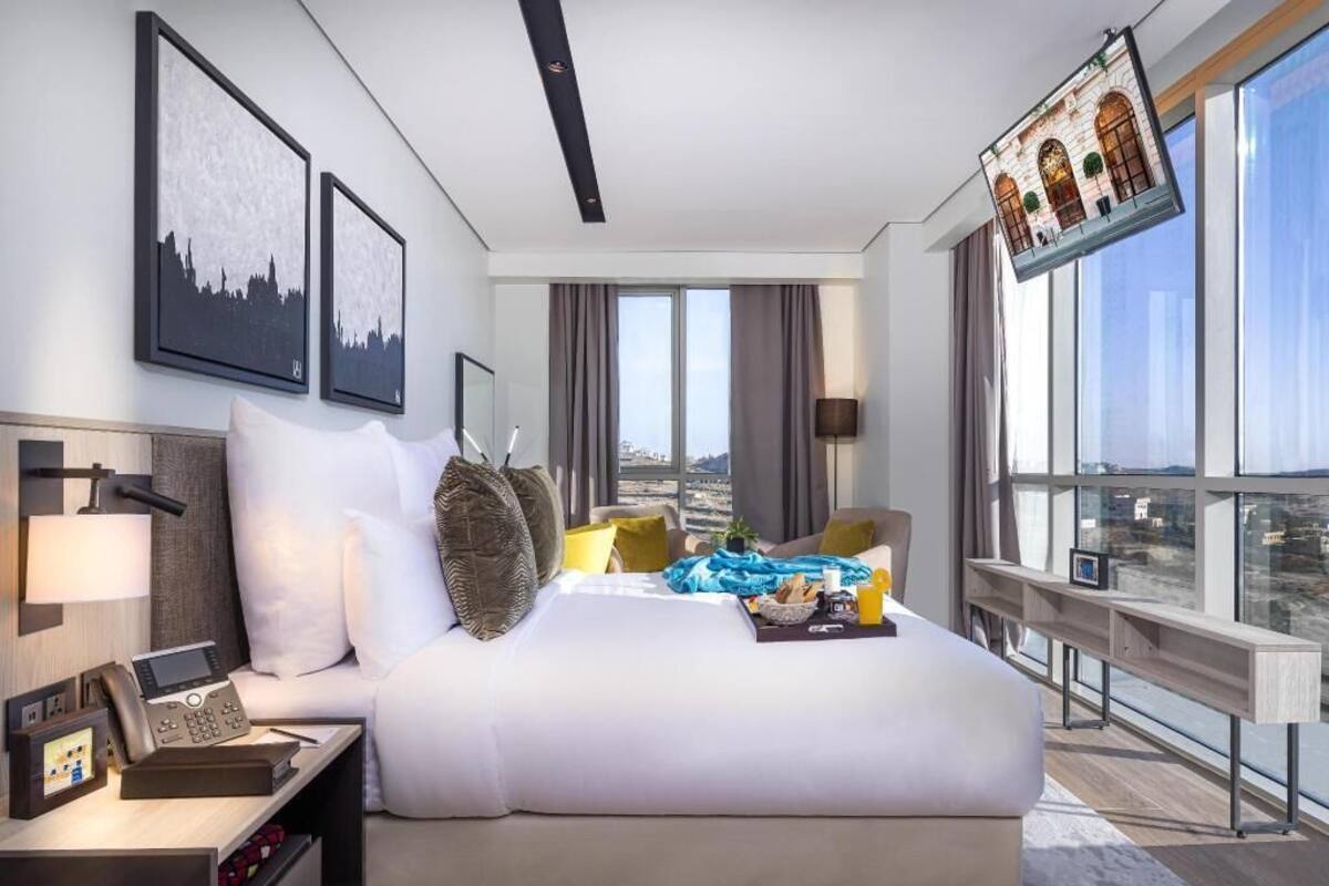 A modern hotel room with a large bed, a desk with a phone, and a city view.